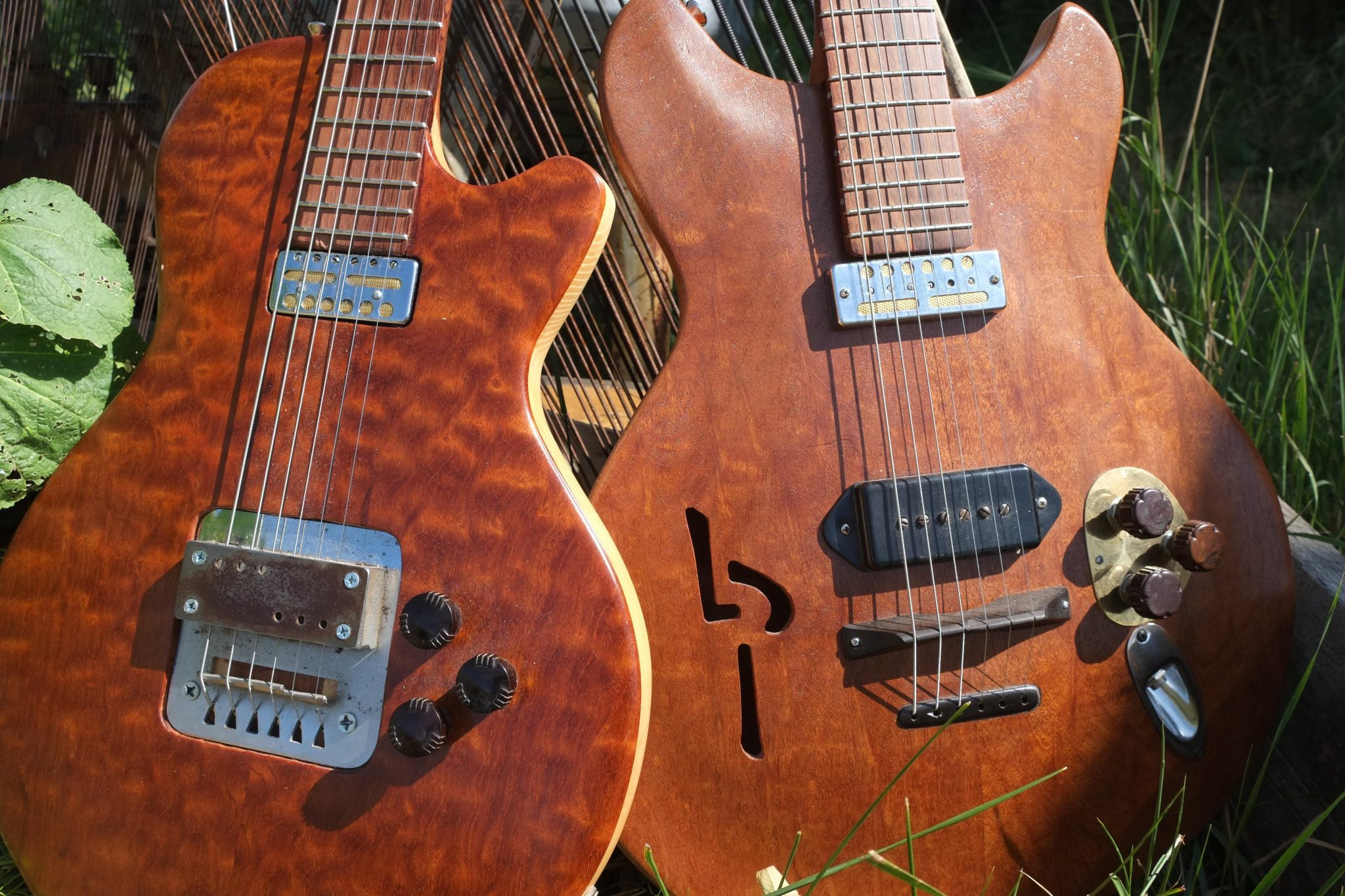 Two electric guitars lean against an old piano harp in the grass. 